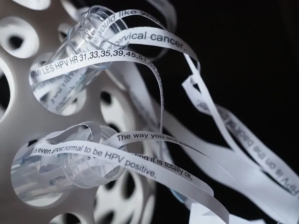 Close-up of plastic tubes with printed messages on paper strips about HPV and cervical cancer awareness.