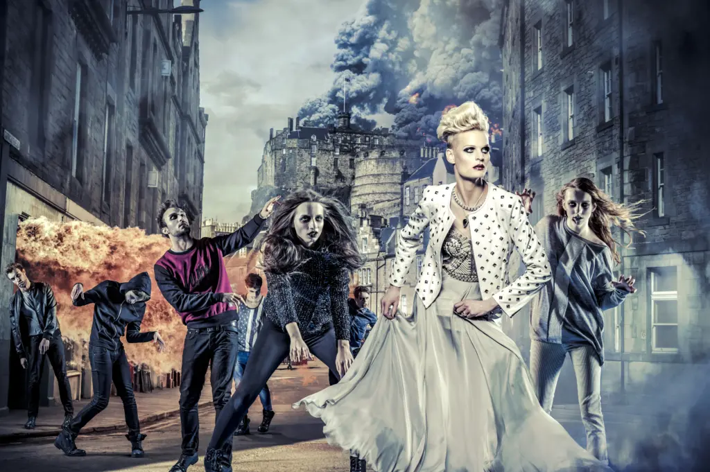 A group of individuals, stylishly dressed, pose dramatically on a street with explosions and smoke in the background, giving the scene a dramatic and chaotic atmosphere.