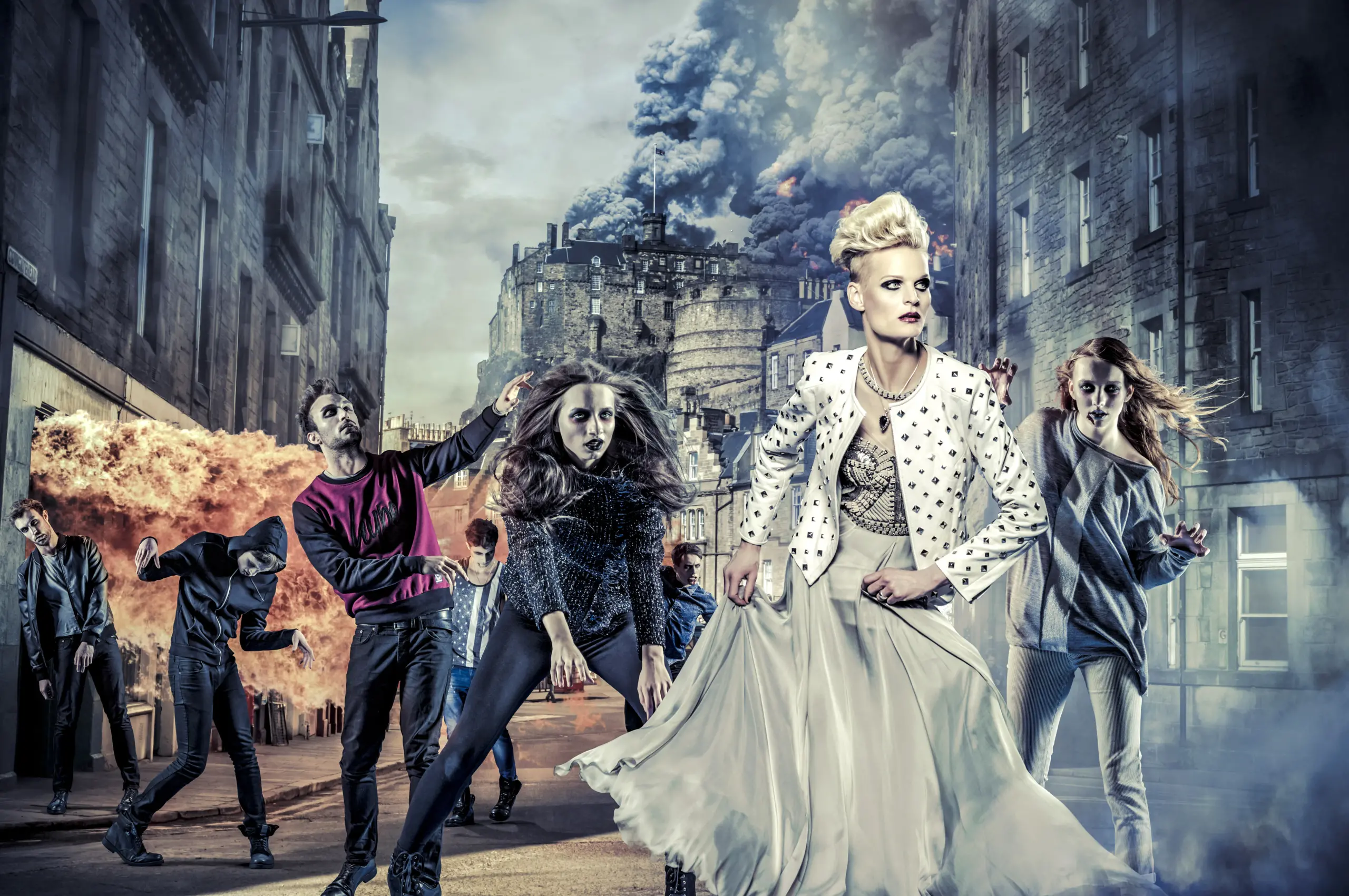 A group of individuals, stylishly dressed, pose dramatically on a street with explosions and smoke in the background, giving the scene a dramatic and chaotic atmosphere.