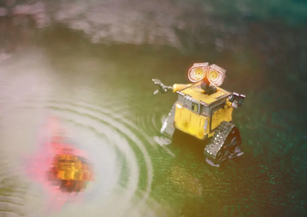 A small, yellow, cartoon-like robot stands in shallow water, creating ripples.