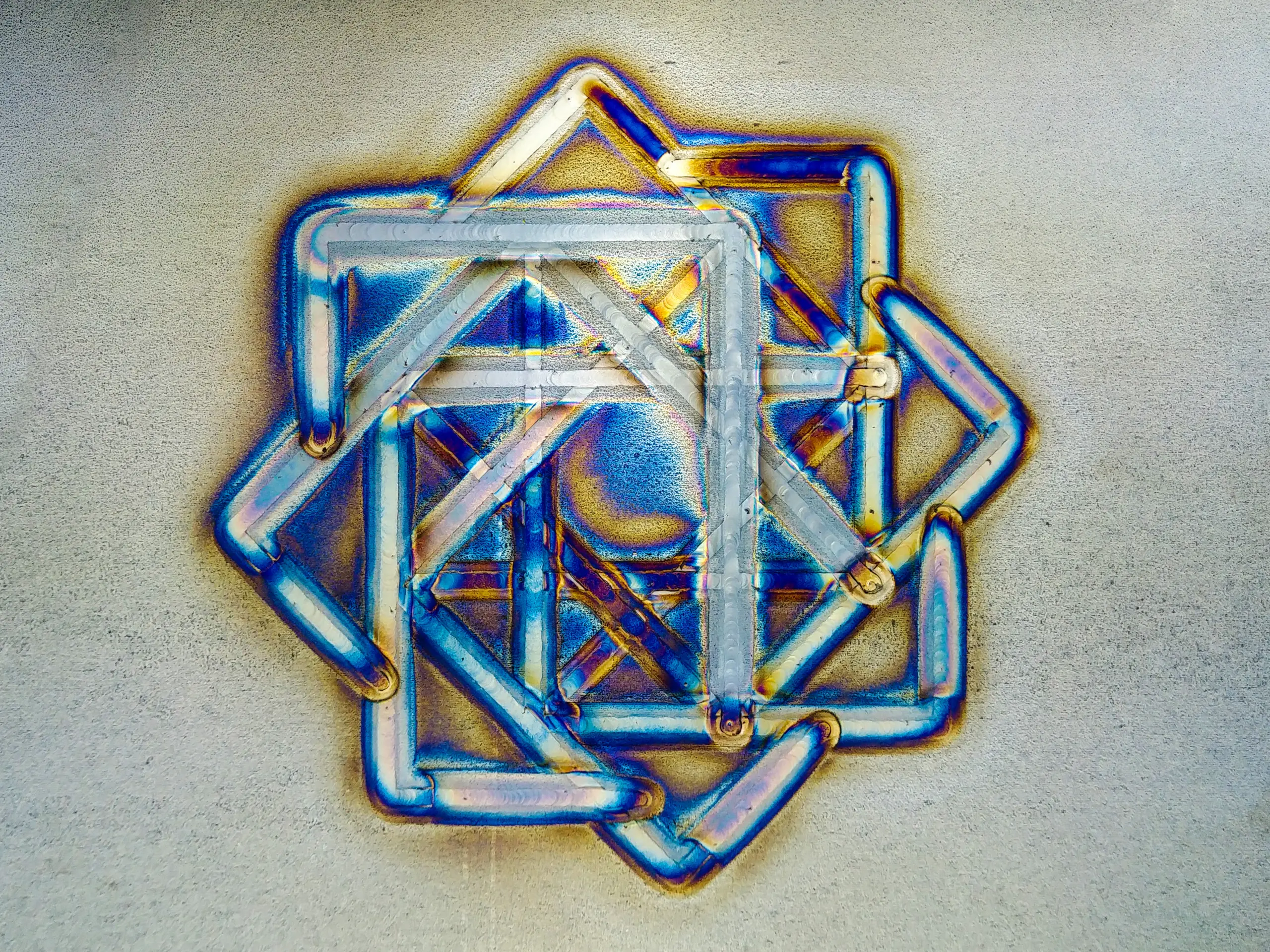 A geometric metal art piece featuring interconnected triangular and square shapes with an iridescent finish.