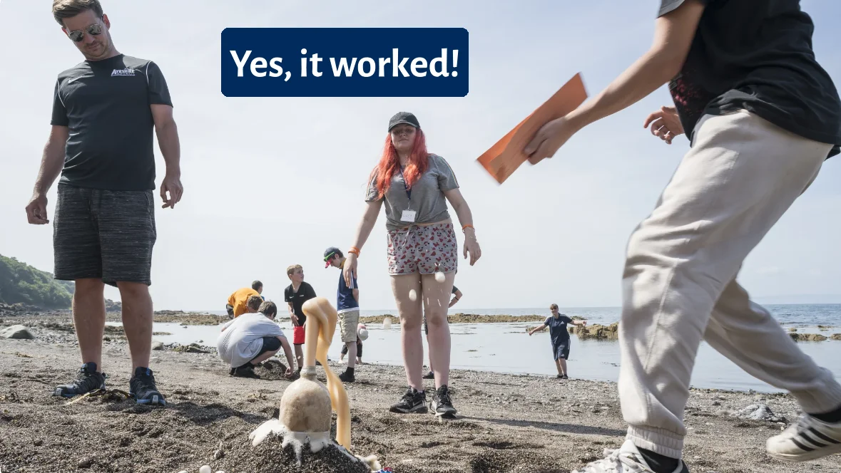 A group of people playing on the beach with a sand sculpture.